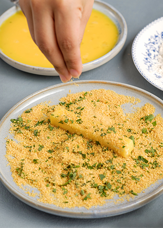 Empanice los bastones de queso con la mezcla del pan molido con extra crunch y el perejil.