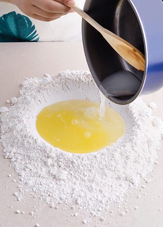 Coloca la harina en una superficie plana y haz un hueco en el centro. Vierte el agua con la mantequilla al centro y agrega sal.