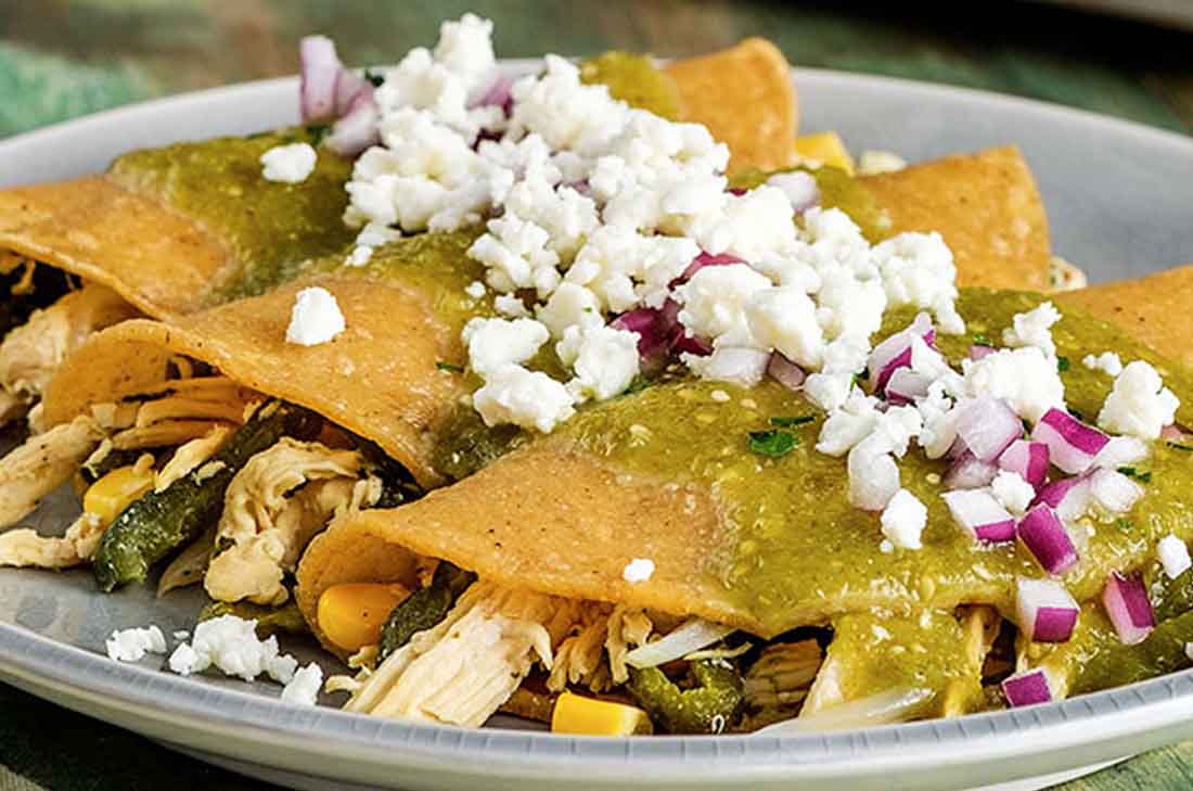 Receta de enchiladas verdes de pollo con rajas de chile poblano y elote acompañadas de queso fresco, crema y cebolla morada