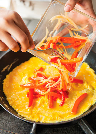 Añade los pimientos, la cebolla y el queso al centro del huevo y cocina por 3 minutos más.
