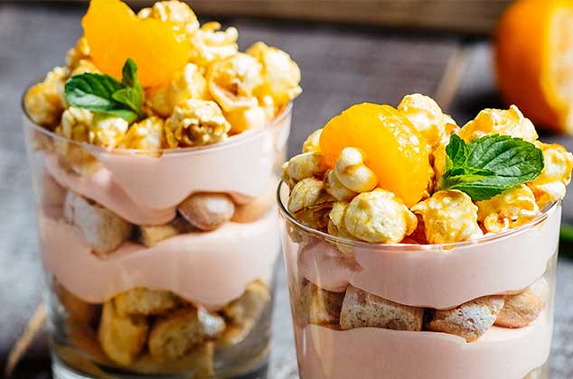 dos vasos de tiramisú con mandarina en la superficie y palomitas de maíz con caramelo y una hoja de menta