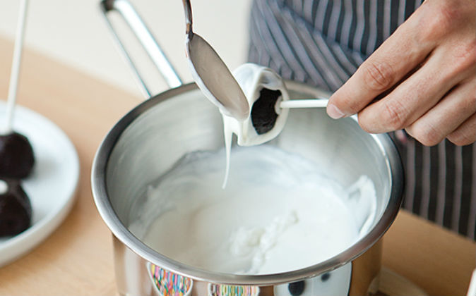 DERRITE a baño María el chocolate blanco. Coloca una gota sobre la bola e introduce el palito de madera. Cubre los cake pops con ayuda de una cuchara. Coloca sobre papel encerado y refrigera por 20 minutos.