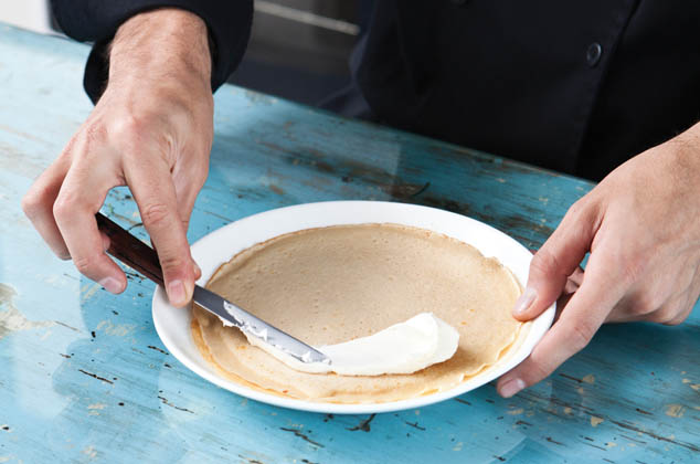 EXTIENDE sobre la crepa una cucharada de queso crema, dobla en cuatro y agrega mermelada de fresa. Decora con trozos de fresa y hojas de meta. 